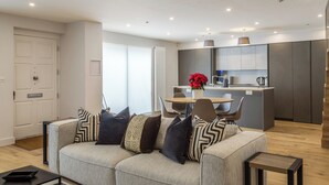 Een moderne woonkamer met een bank, een eettafel en een keuken met een koelkast en een koffieapparaat.