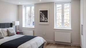 Een slaapkamer met een bed, twee ramen, een radiator en een aan de muur hangend schilderij.