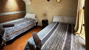 A room with two beds, a brick wall, a wooden ceiling, and a tiled floor.