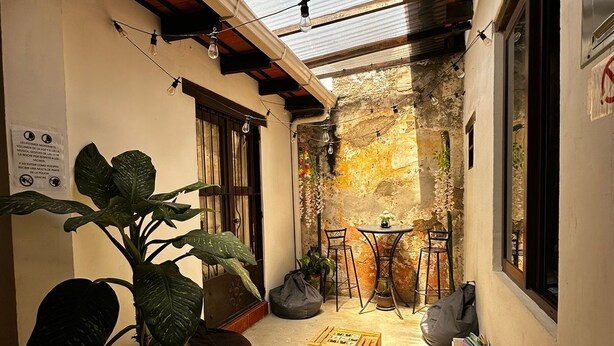 A narrow alleyway with a small table and chairs, a potted plant, and a wooden crate.