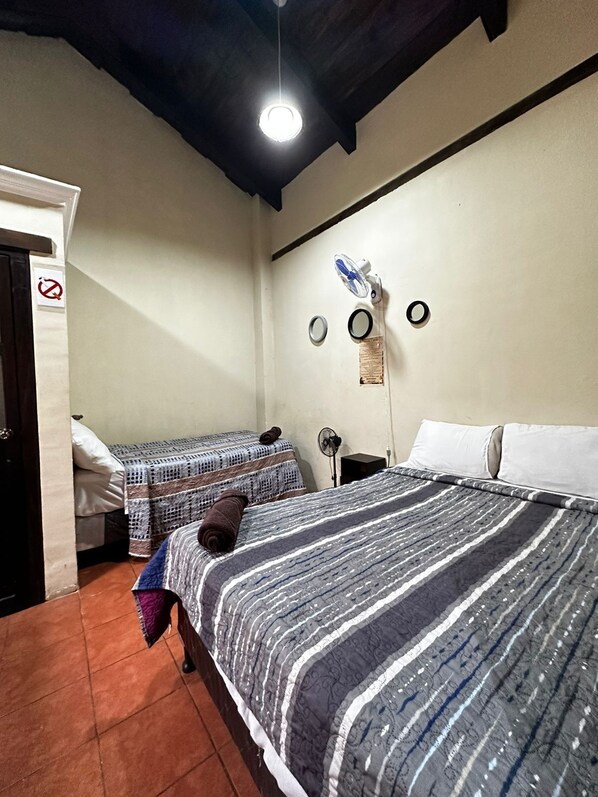 A room with two beds, a ceiling fan, and a light fixture. - El Aventurero GT (Antigua Guatemala)