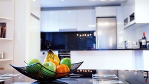 A modern kitchen with white cabinets, a black countertop, and a fruit bowl containing apples, bananas, and oranges.