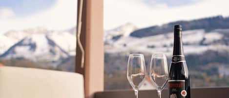 A bottle of Heldenblut wine, two empty wine glasses, and an orange on a table with a mountain view in the background.