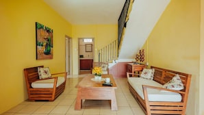 A bright yellow room with wooden furniture, a painting, and a staircase.