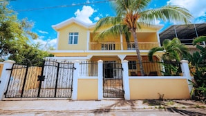 A two-story house with a balcony, a gated entrance, and a palm tree in the yard.