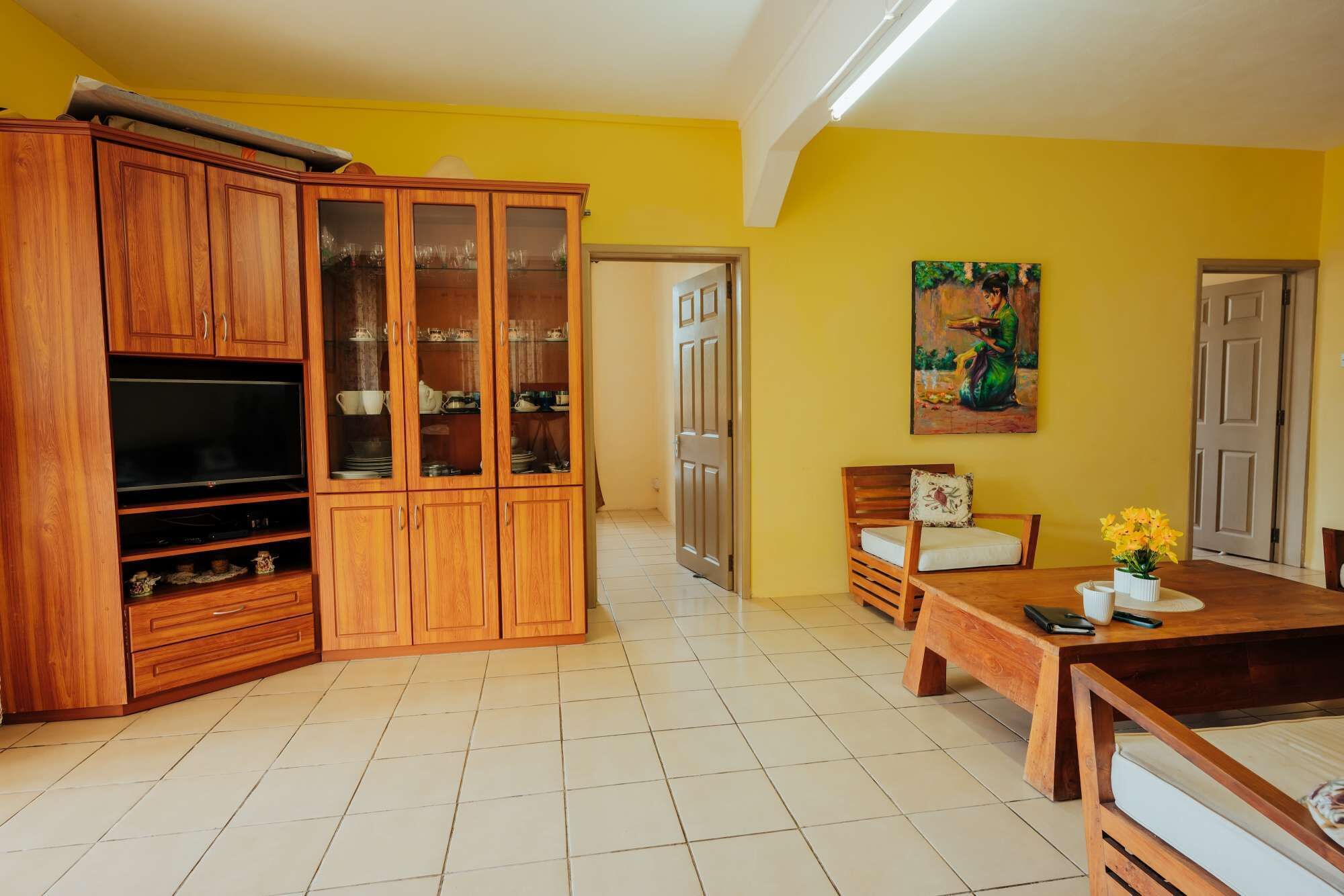 A living room with a wooden cabinet, a television, a dining table with chairs, and a painting on the wall.