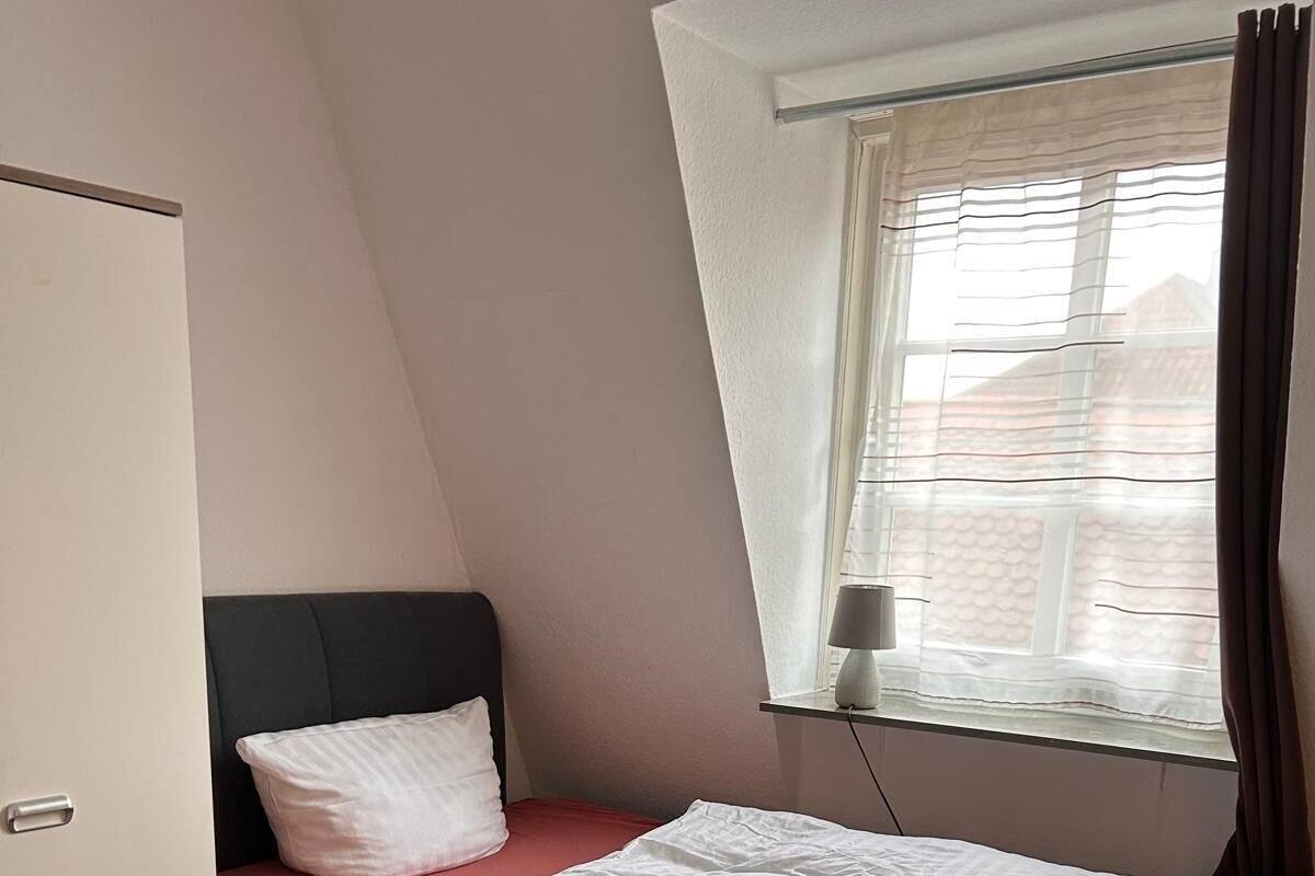 A single bed with a red mattress and white bedding, a bedside lamp, and a window with curtains.