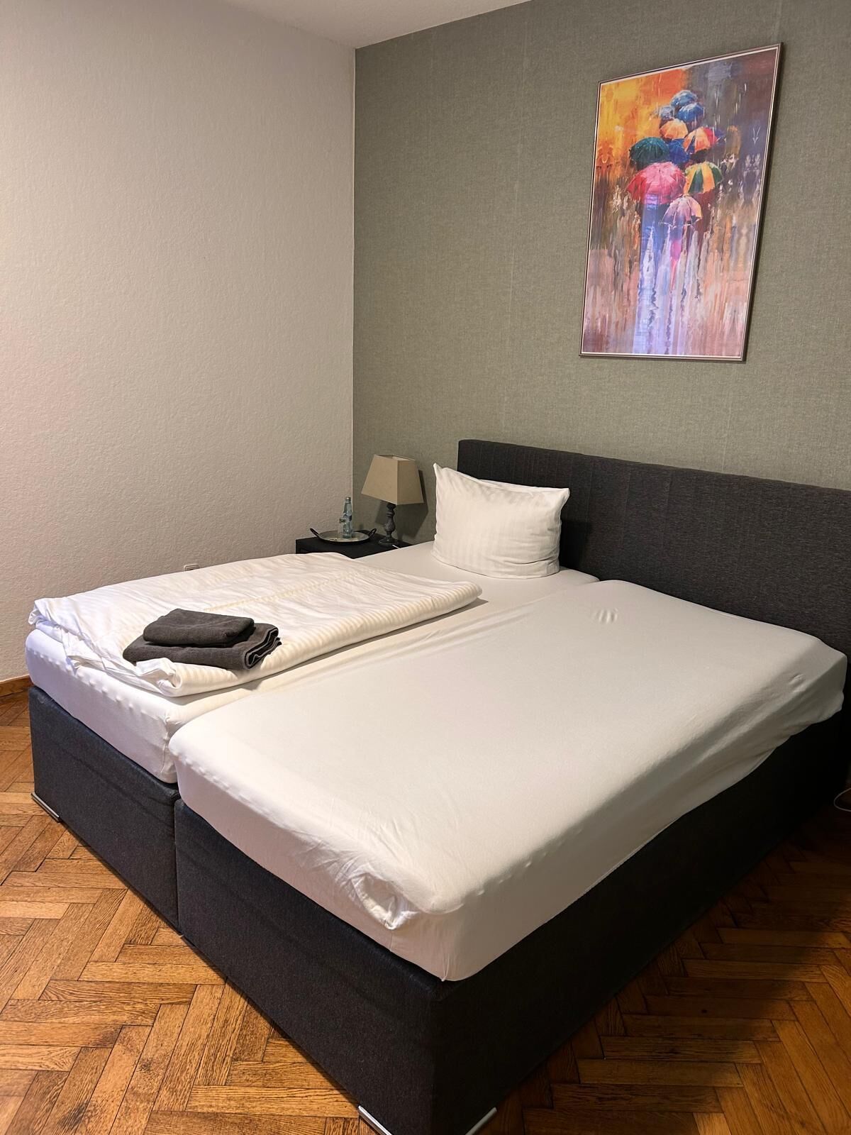 Ein ordentlich bezogenes Bett mit weißer Bettwäsche, einem dunklen Kopfteil und einem Gemälde an der Wand.