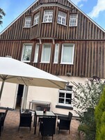 Un edificio con fachada de madera y varias ventanas. Cuenta con un patio con mobiliario exterior y una mesa.