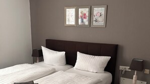 A double bed with white linens, a dark headboard, and a nightstand with a lamp.