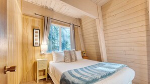 Un dormitorio con cama, mesita de noche, ventana con cortinas y puerta con manija.