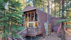 Una cabaña con fachada de madera, base de piedra y una escalera que conduce a una terraza.