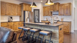 Een moderne keuken met houten kastjes, een centraal kookeiland met barkrukken, roestvrijstalen apparatuur en hangende lampen.