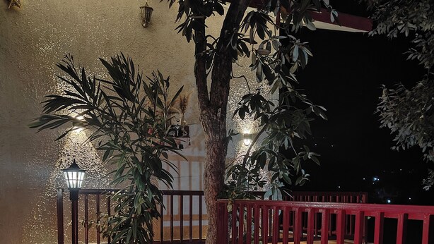 A fire pit with flames, surrounded by a red fence and potted plants. - DeerWood Cottages (Tehri)