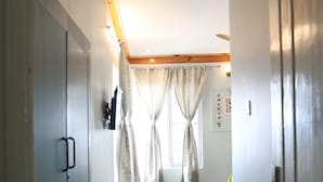 A hallway with wooden beams, a door on the left, a window with curtains, and a rug on the floor. - DeerWood Cottages (Tehri)