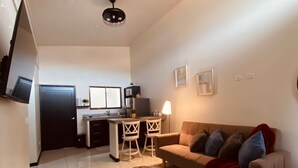 Ein modernes Wohnzimmer mit Sofa, Hocker und einer Küche im Hintergrund.