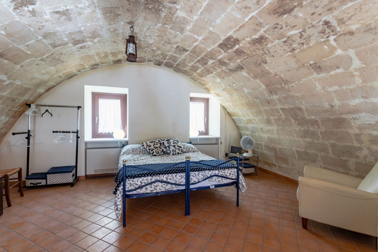 A bedroom with a sloped ceiling, a bed with a patterned bedspread, a chair, a small table, and a window.