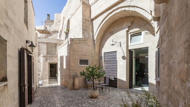 A narrow alleyway with stone flooring, a small tree, and a glass door leading to a building. - GuestHost - Domus Tua (Matera)