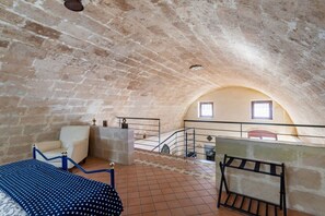 A high-ceilinged room with a sloped ceiling, a bed, a chair, a small table, and a window.