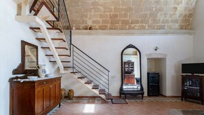 A spacious living area with a staircase, a wooden cabinet, a mirror, a television, and a fireplace. - GuestHost - Domus Tua (Matera)