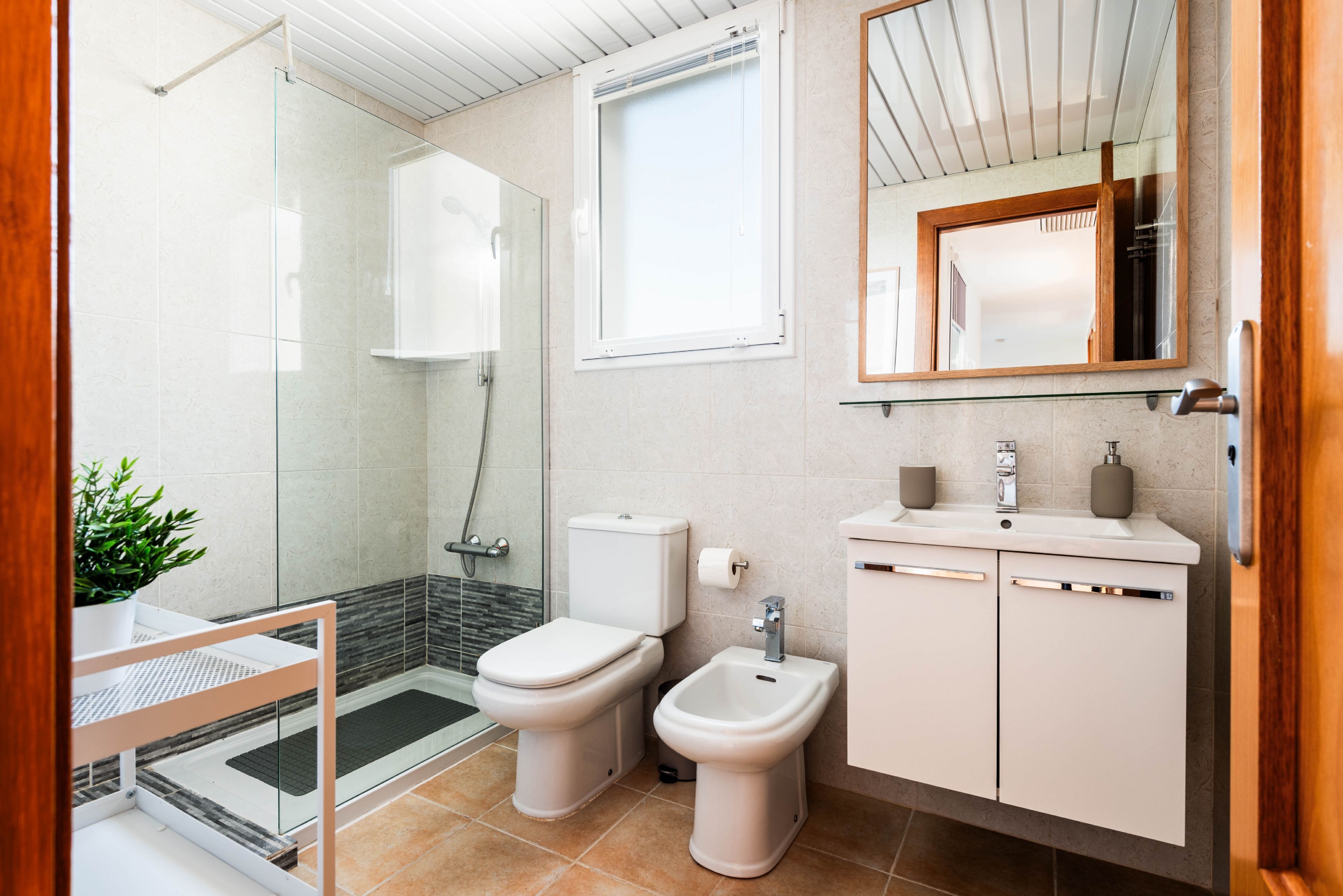 A modern bathroom with a glass shower enclosure, a toilet, bidet, and a sink with a mirror above.