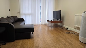 A living room with a black sofa, a TV on a wooden stand, and a radiator. - City Central Apartment  (Birmingham)