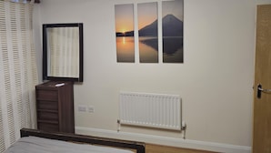 A bedroom with a bed, a dresser, a radiator, and a wall-mounted picture of a sunset over a mountain. - City Central Apartment  (Birmingham)
