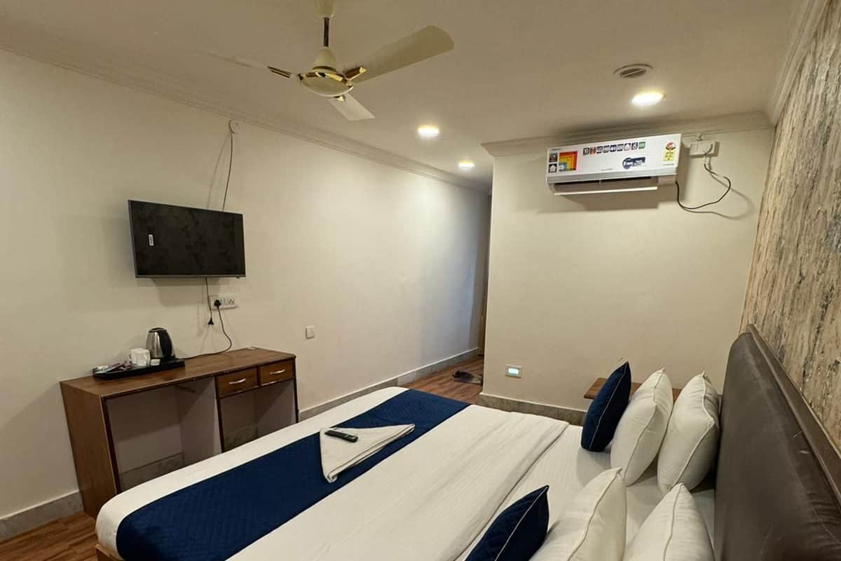 Quarto de hotel com cama, escrivaninha, televisão e ar condicionado.