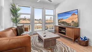 Una sala de estar con un sofá de cuero, una mesa de centro, un televisor sobre un soporte de madera y vistas a un paisaje desértico a través de grandes ventanales.