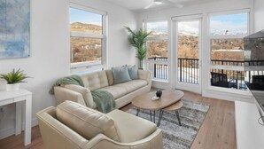A modern living room with a beige sofa, a round coffee table, and a view of a mountainous landscape through large windows. - INCREDIBLE Views Capital +MTN+City! Penthouse cnr suite! Best Amenities! (Salt Lake City)