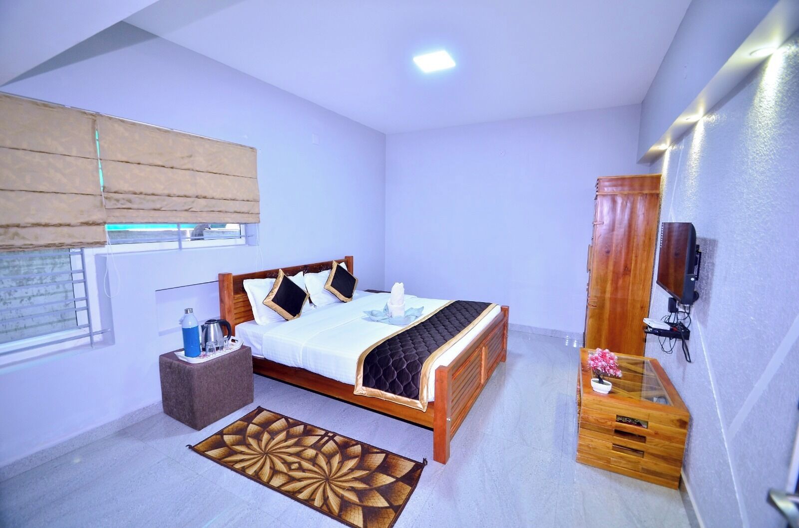 A bedroom with a wooden bed, a bedside table, a TV, and a window with blinds.