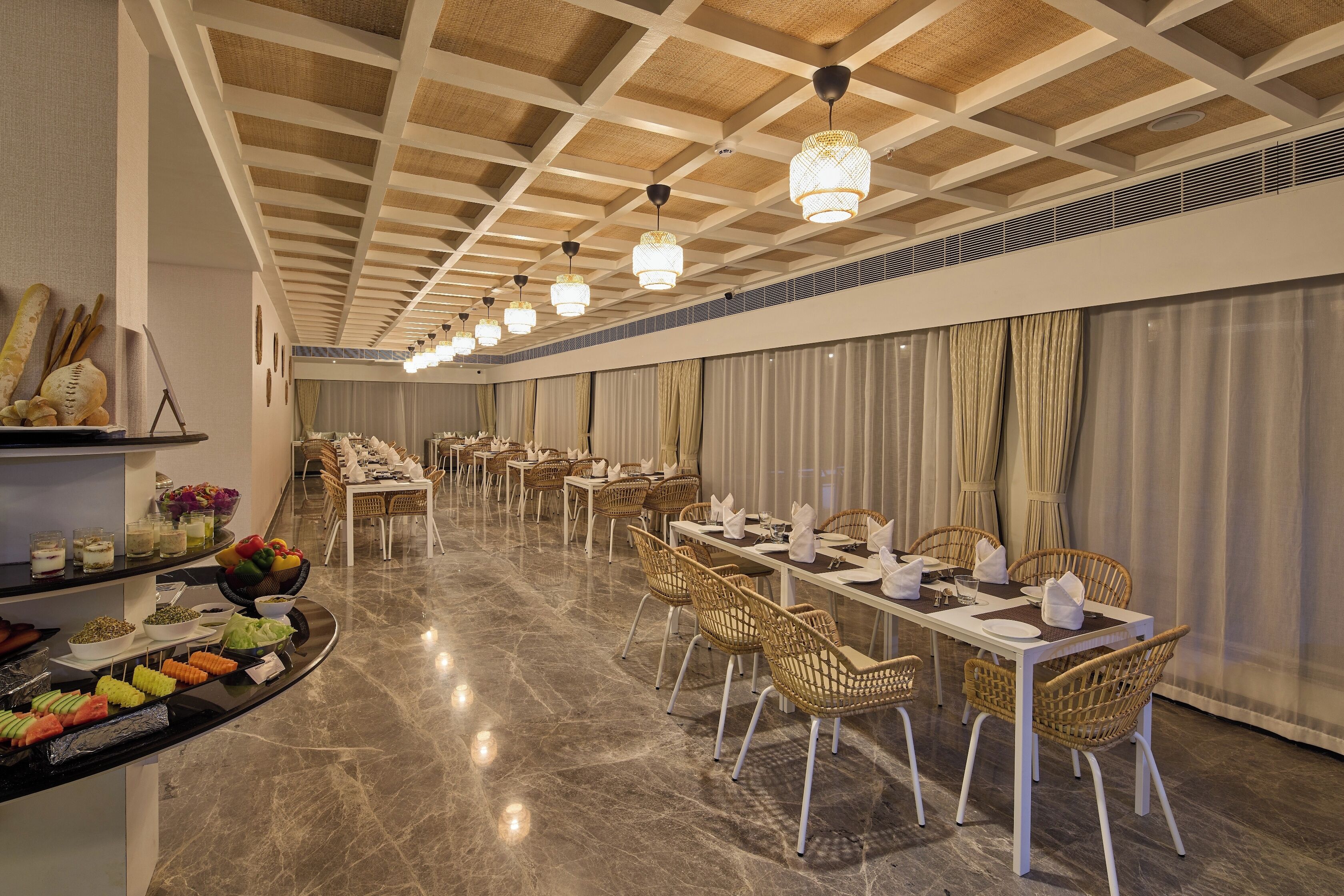 A spacious dining area with long tables, wicker chairs, and a buffet with various food items.