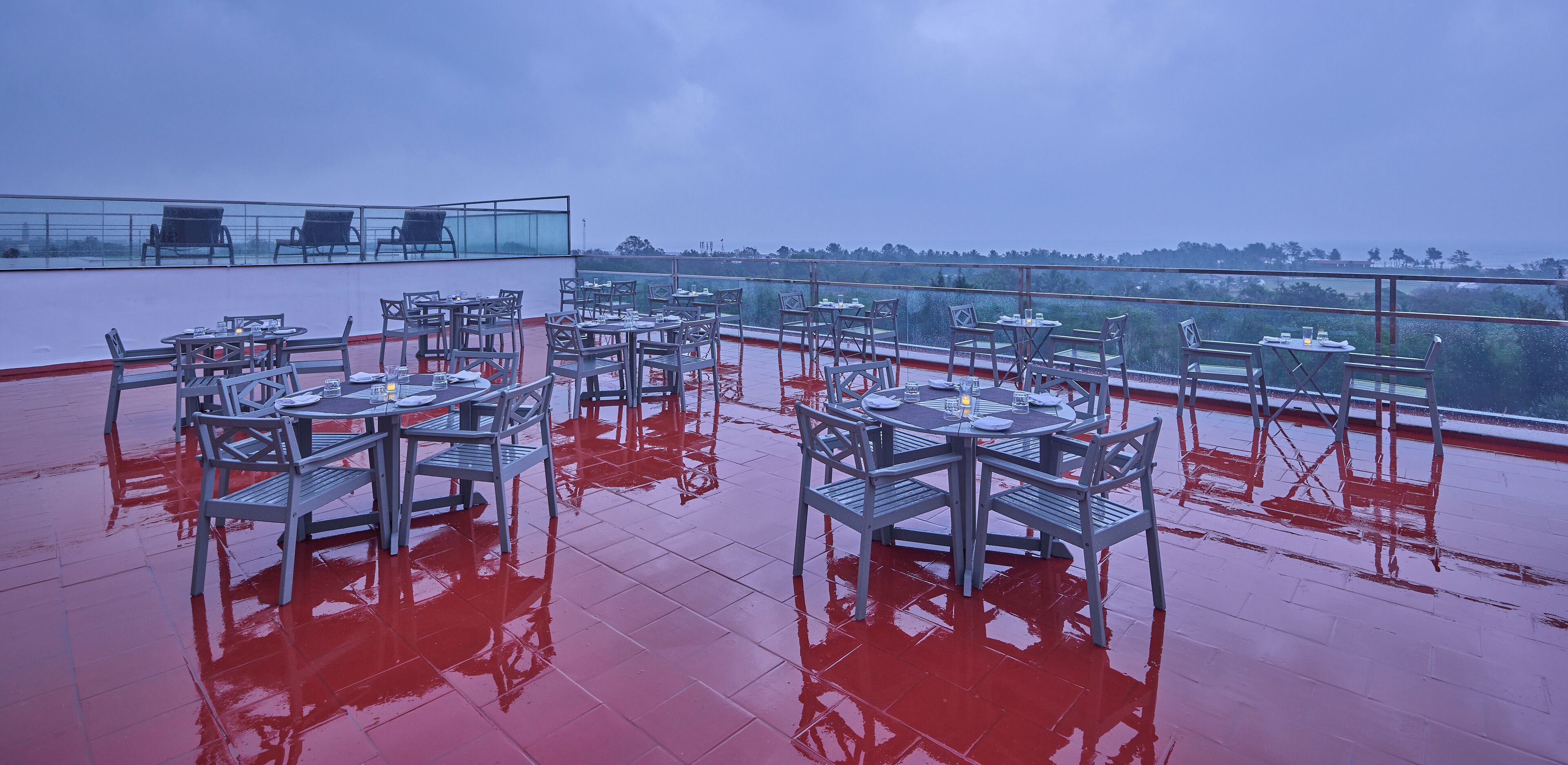 Une terrasse sur le toit, avec des tables et des chaises, une rambarde en verre et une vue sur l’horizon.