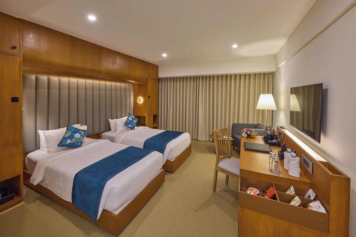 Une chambre d’hôtel avec deux lits, un bureau avec une lampe, une télévision et un mini-bar.