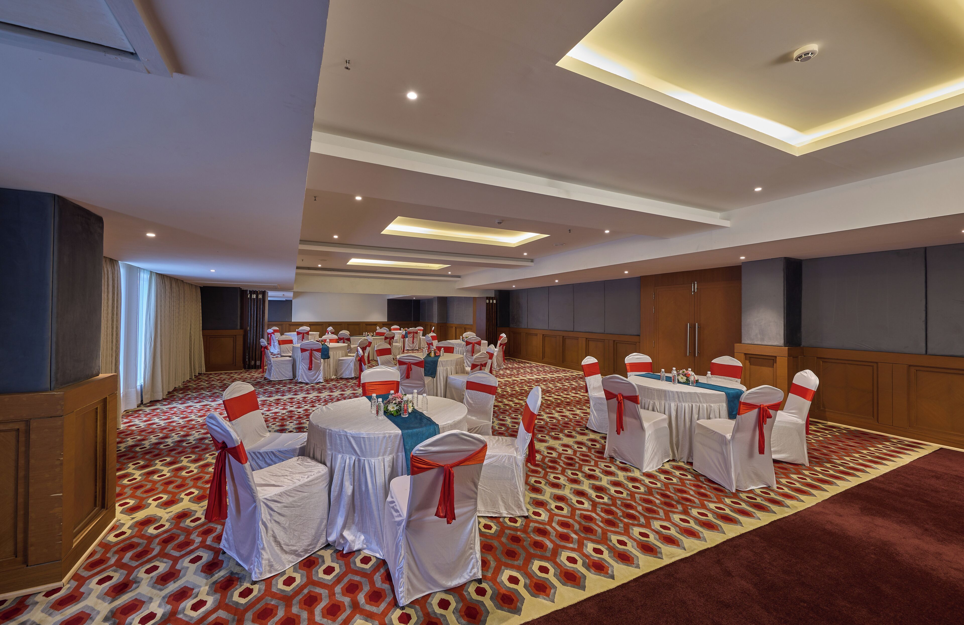 A large conference room with round tables, white chairs with red sashes, and a patterned carpet.
