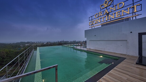 Une piscine sur le toit offrant une vue sur le paysage urbain, une enseigne indiquant « Grand Continental » et une terrasse en bois entourant la piscine.
