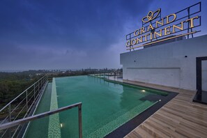 Una piscina en la azotea con vistas al paisaje urbano, un letrero que dice "Grand Continental" y una terraza de madera alrededor de la piscina.