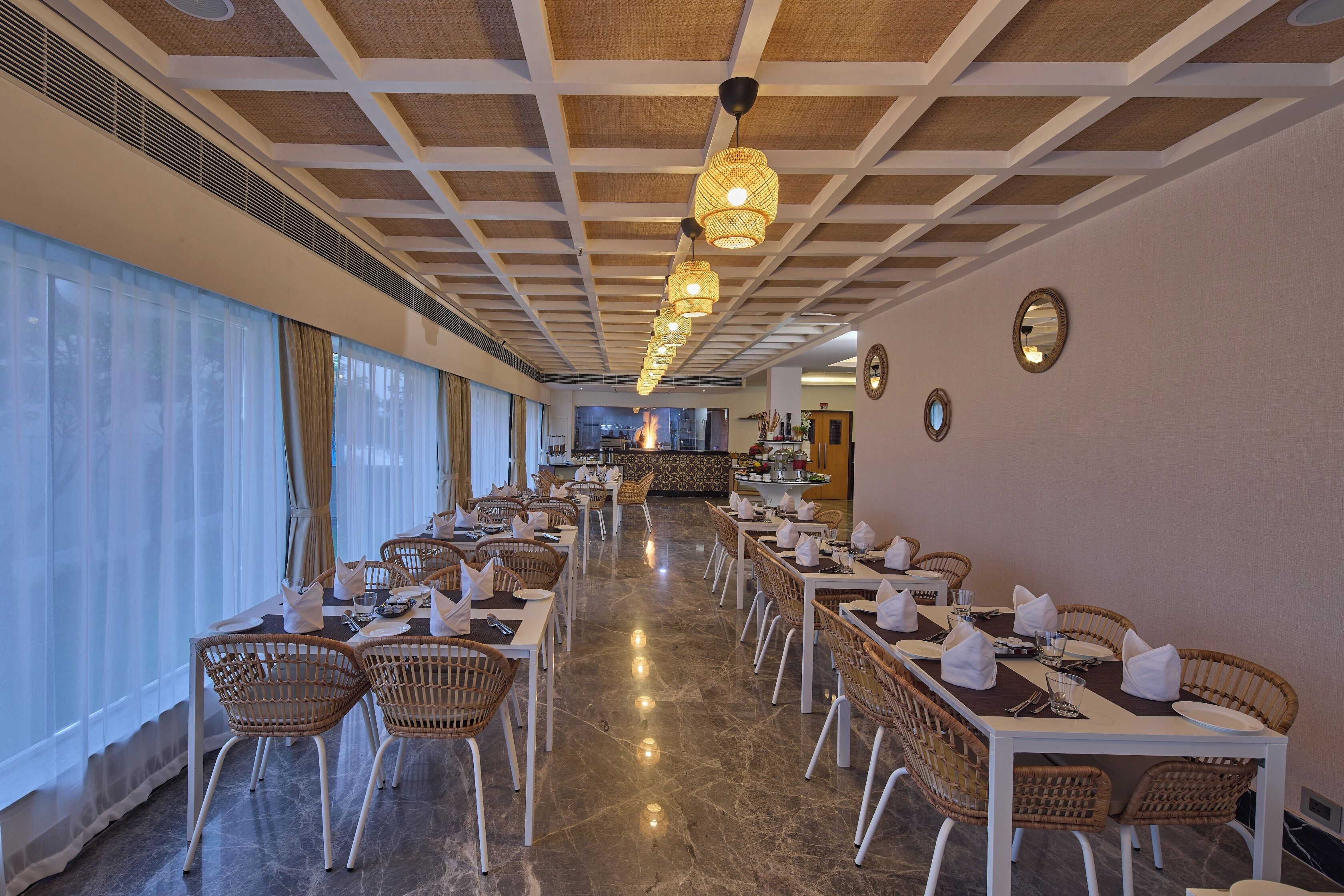 A spacious dining area with long tables, wicker chairs, and hanging pendant lights.
