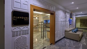 Un hall d'hôtel avec une enseigne indiquant « RESTAURATION SUR PLACE », une cloison en verre, un comptoir d'accueil et un mur décoratif orné de motifs complexes.