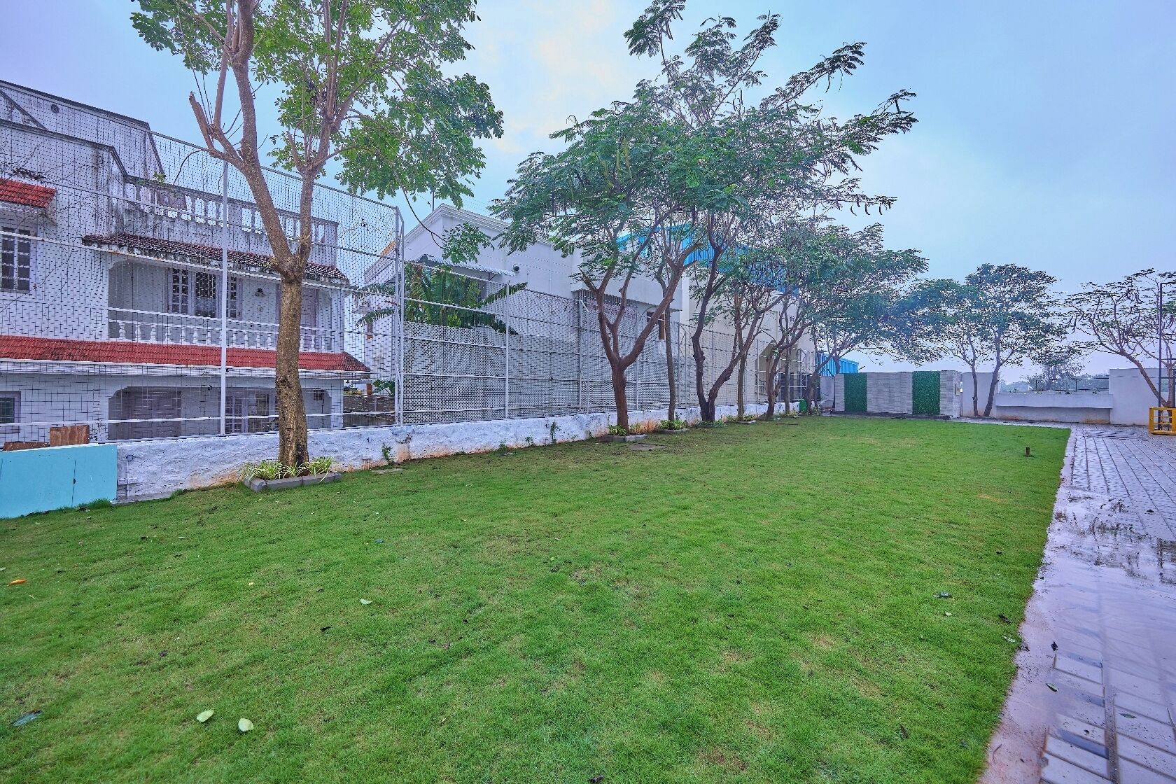 A grassy courtyard with a white building, trees, and a blue wall.