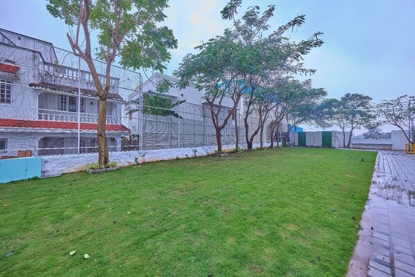Un patio cubierto de césped con un edificio blanco, árboles y un muro azul.