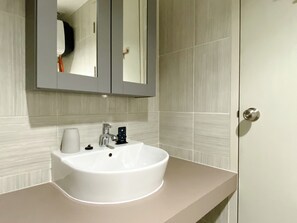 Bathroom features a sink, mirror, and door with a silver handle, set against a backdrop of light-colored tiles.