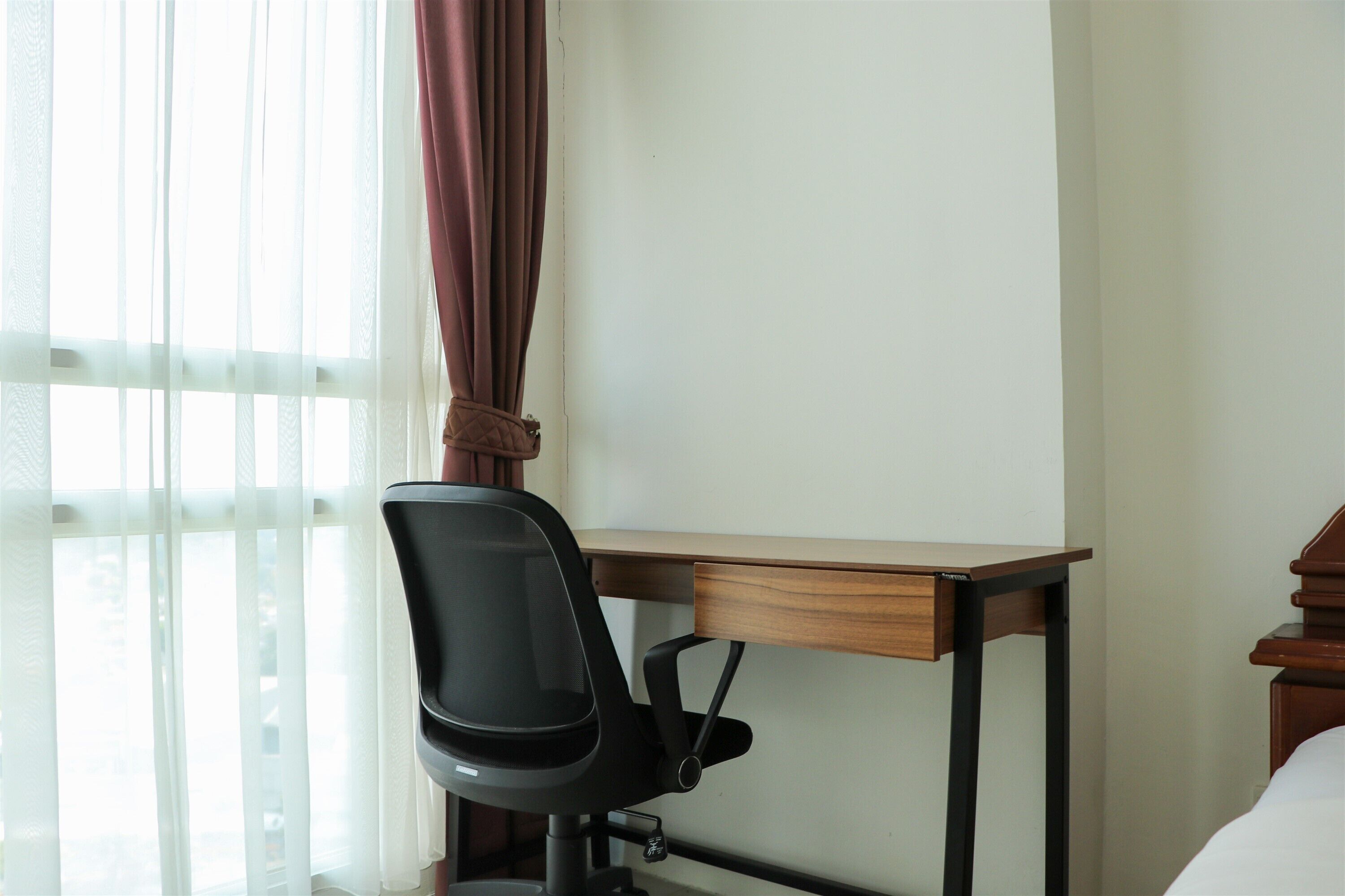 A hotel room with a wooden desk, a black office chair, and a bed.