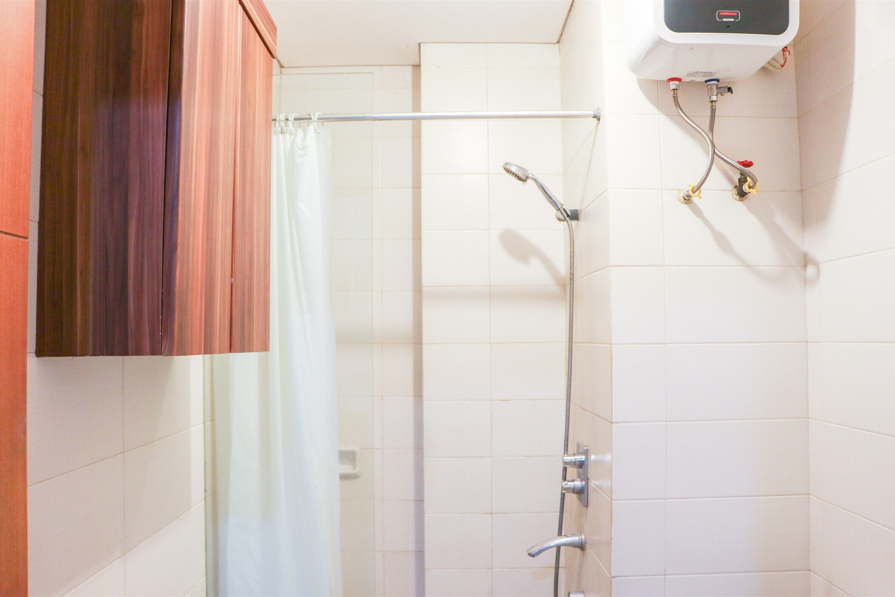 Un espace douche équipé d’un pommeau de douche en métal, d’un rideau et d’un chauffe-eau fixé au mur.