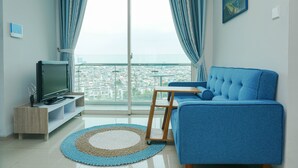 A modern living room with a large window, a sofa, a TV, and a small table. - Elegant And Spacious 1Br At Citralake Suites Apartment (Jakarta)