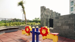 Outdoor play equipment with a stone wall and a palm tree in the background. - Elegant And Spacious 1Br At Citralake Suites Apartment (Jakarta)