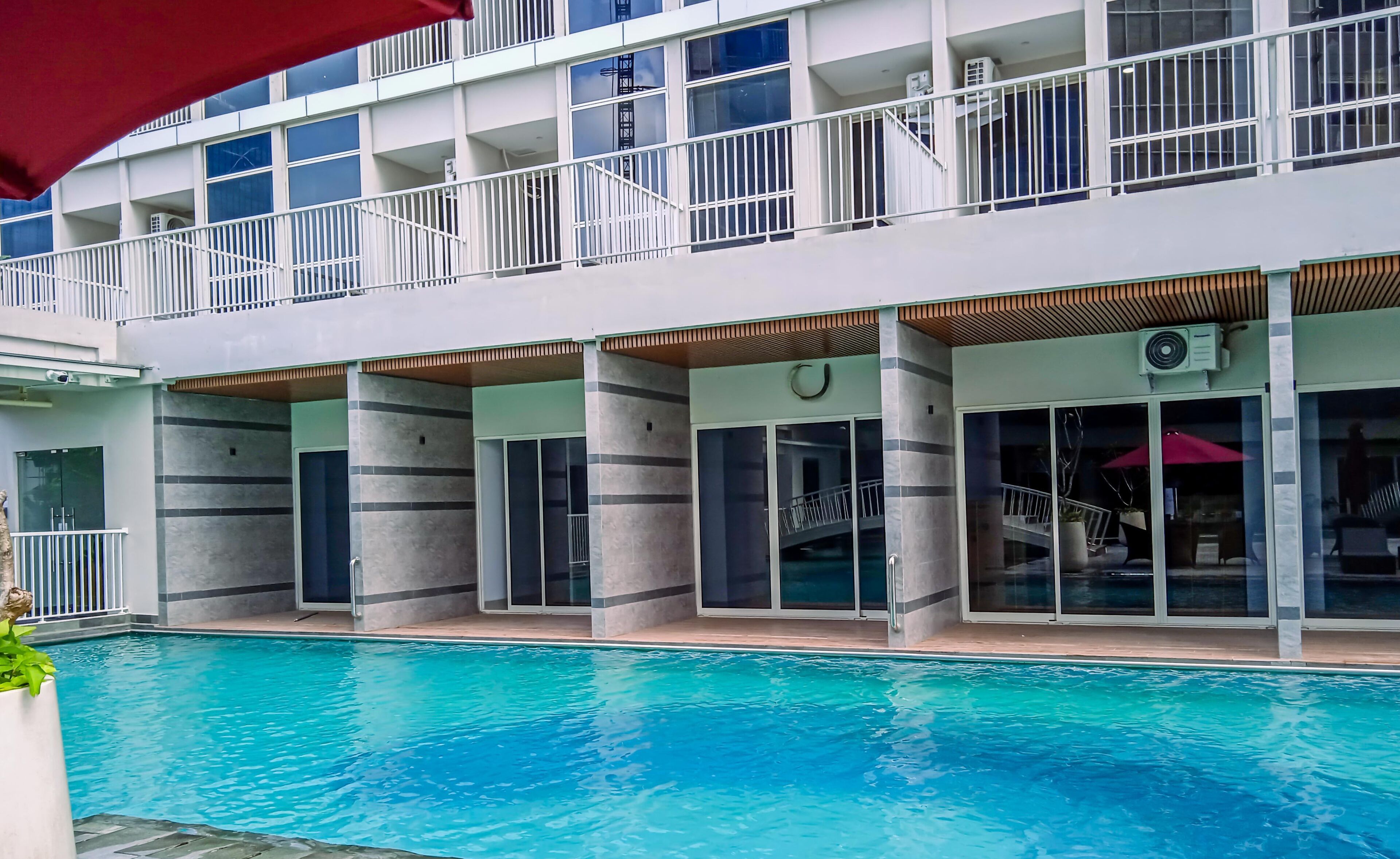 A modern hotel with a pool area, featuring a two-story building with balconies, large windows, and a covered seating area.