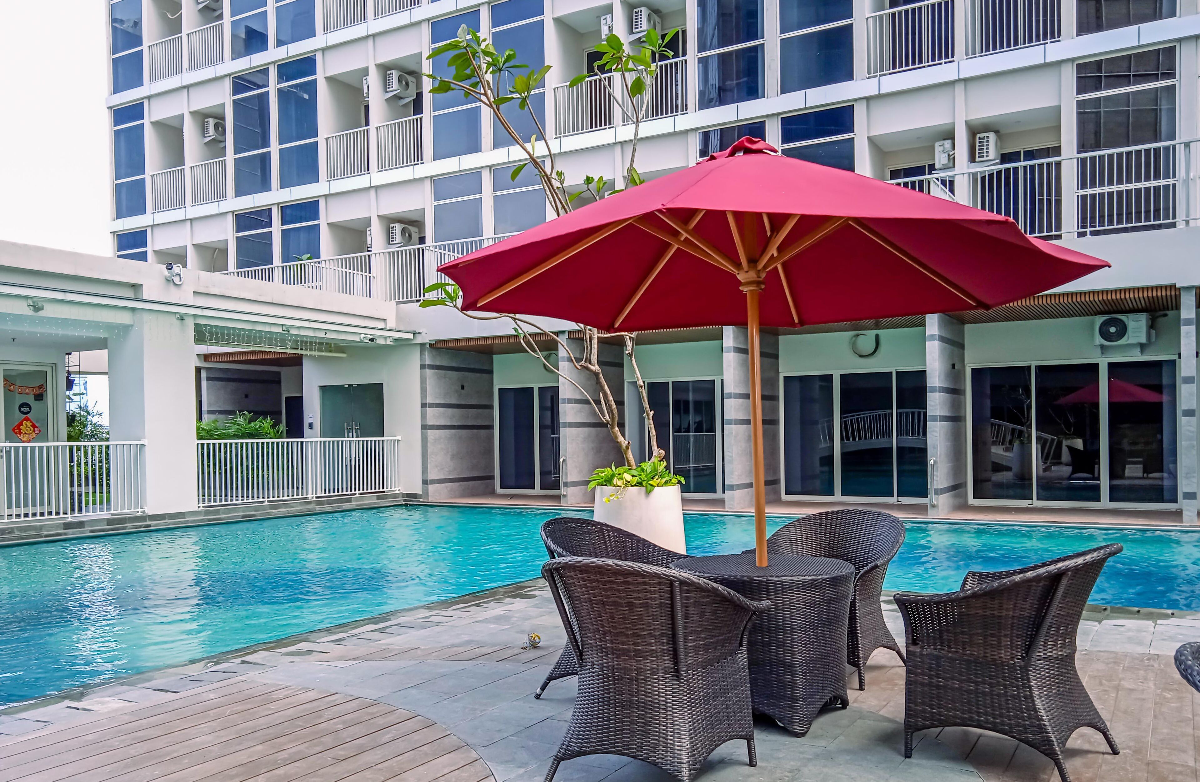 An outdoor swimming pool area with wicker furniture and a red umbrella.