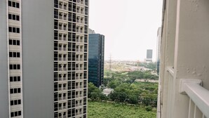 A high-rise building with multiple floors and balconies, a modern glass facade, and a view of a green park area with trees and a road. - Best Deal Studio Pacific Garden Apartment Alam Sutera (Tangerang)