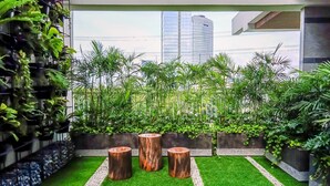 A modern outdoor space with artificial grass, wooden planters, and a variety of green plants. - Best Deal Studio Pacific Garden Apartment Alam Sutera (Tangerang)